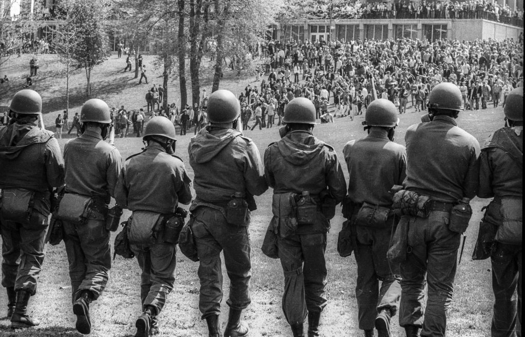 View, from behind, of Ohio National Guardsmen in gas masks and with rifles as they advance up Blanket Hill to back Kent State University students during an antiwar demonstration on the university's campus, Kent, Ohio, May 4, 1970. The protests, initially over the U.S. invasion of Cambodia, resulted in the deaths of four protesters (and the injuries of nine others) after the National Guard opened fire on students. Photo by Howard Ruffner/Getty Images