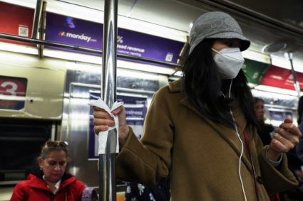 A woman wearing a protective face mask holds on to a subway pole with a napkin in New York City