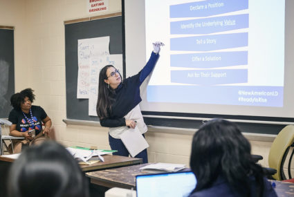 Ghida Dagher, President and CEO of New American Leaders, shares her expertise at a Ready to Lead® National Women's Training, woman standing in front of a classroom pointing at a powerpoint screen
