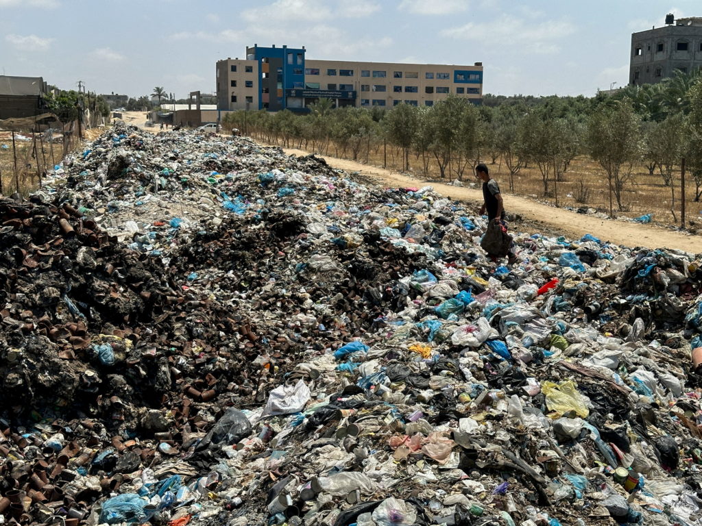 Palestinian man walks on piles of garbage, in Deir Al-Balah