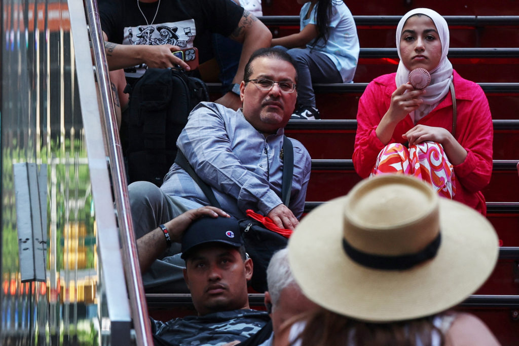 A woman cools herself off with a fan while sitting down in the Time Square area of New York City