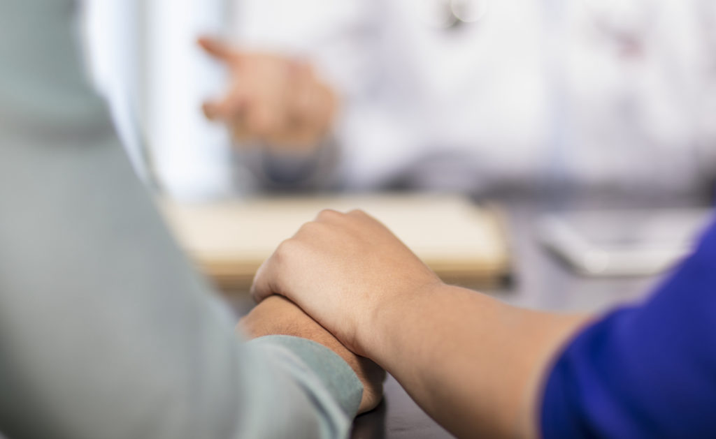 Doctor and couple holding hands in medical practice