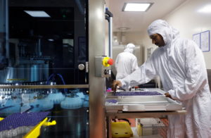 An employee in personal protective equipment (PPE) collects vials of the R21 malaria vaccine after they come out from a vi...