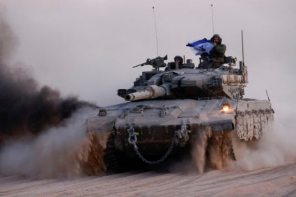 Soldier holds an Israeli flag, while riding on a tank, near the Israel-Gaza border