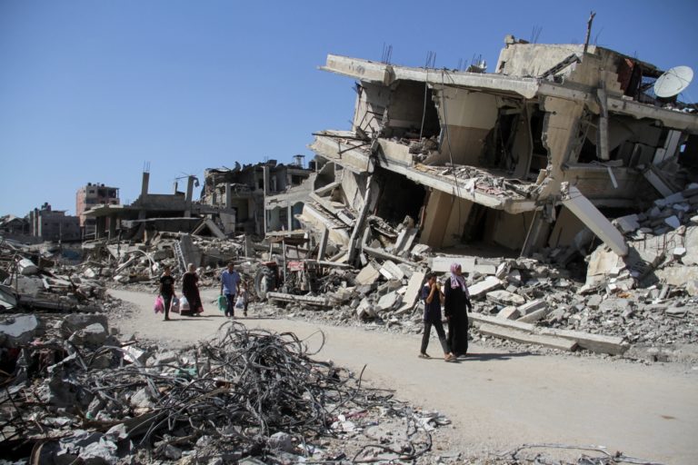 Palestinians walk among the rubble of damaged buildings, in Beit Lahia