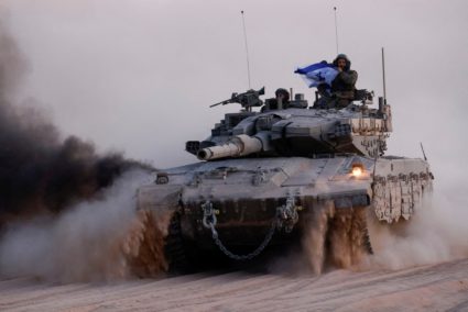 Soldier holds an Israeli flag, while riding on a tank, near the Israel-Gaza border