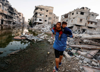 A Palestinian man holds his children as he walks next to buildings destroyed in an Israeli strike, in Khan Younis