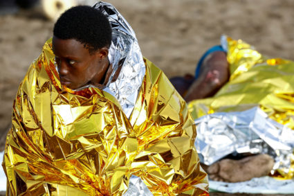 Two migrants rest on the sand after arriving in a fiber boat at Las Burras beach in San Agustin