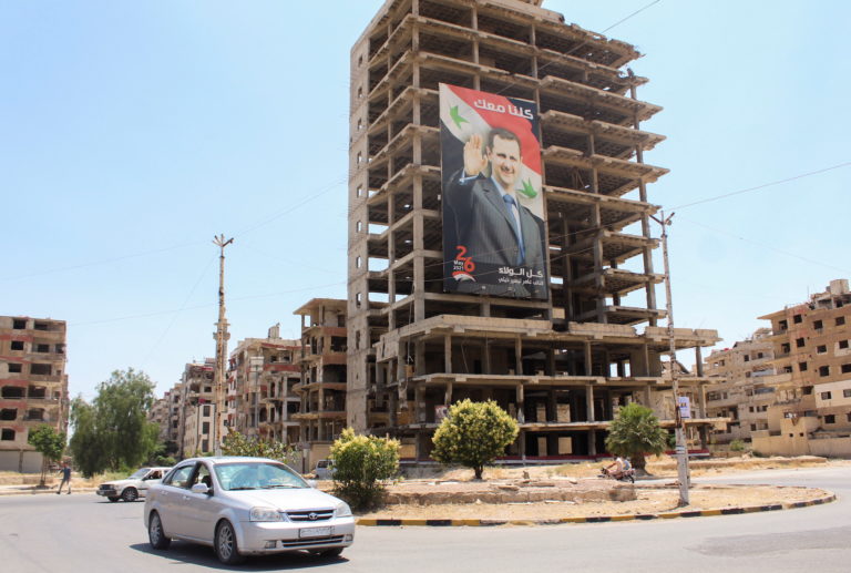 Vehicles pass near a poster depicting Syria's President Bashar al-Assad in Douma