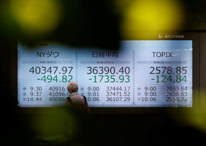 A man looks at an electronic screen displaying Japan's Nikkei, Topix share averages and the Dow Jones Industrial Average o...