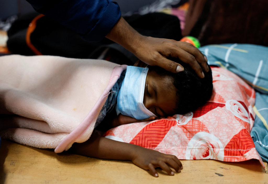 Man pats his son's head, after he caught a high fever inside a relief camp, following landslides that hit several villages...
