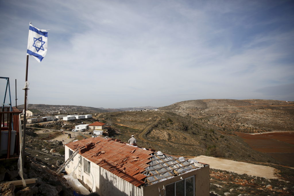 An Israeli flag flutters as a Jewish settler works on the construction of a house in the unauthorised Jewish settler outpo...