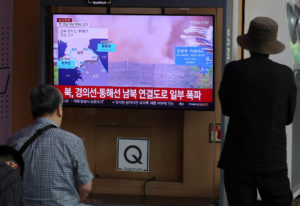 People watch a TV broadcasting a news report on North Korea blowing up sections of inter-Korean roads and rail lines on it...