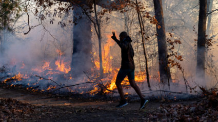 A morning jogger gestures as he runs past a fire lit by members of the New Jersey Forest Fire Service as it burns alongsid...