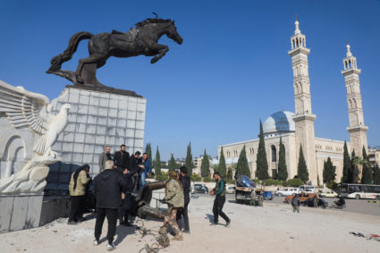 People and Syrian opposition fighters stand at a damaged statue in Al Basel square in Aleppo