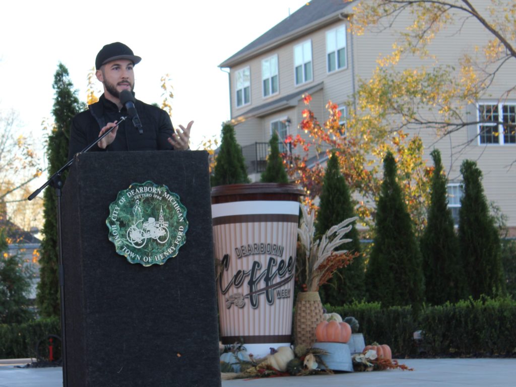 mayor abdullah hammoud standing behind a podium with a giant coffee cup behind him for Dearborn Coffee Week