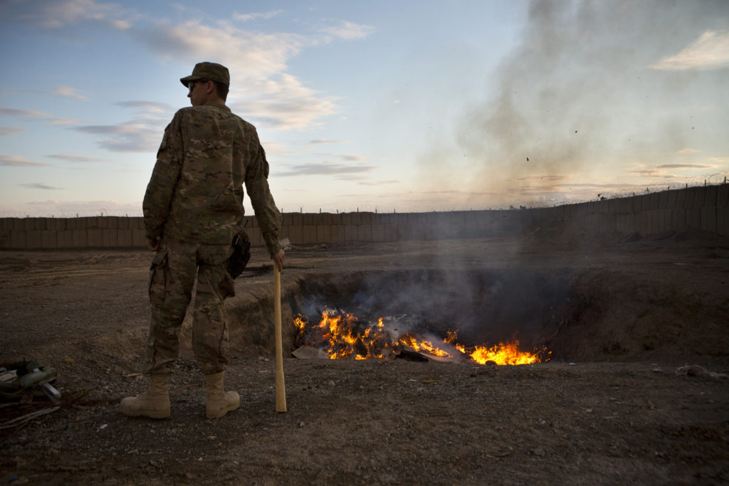 A U.S. Army soldier watches bottled water that had gone bad burn in a burn-pit at Forward Operating Base Azzizulah in Maiw...