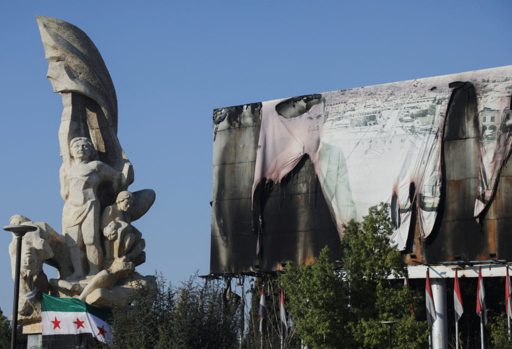 Syrian Opposition flag is placed near a burnt banner of Syria's President Bashar al-Assad in Aleppo