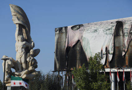 Syrian Opposition flag is placed near a burnt banner of Syria's President Bashar al-Assad in Aleppo