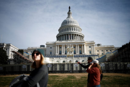 People walk past the U.S. Capitol with an inaugural platform under construction in front of it, in Washington