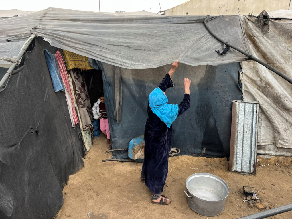 A displaced Palestinian woman adjusts her tent cover on a rainy day, amid the Israel-Hamas conflict, in Khan Younis in the...