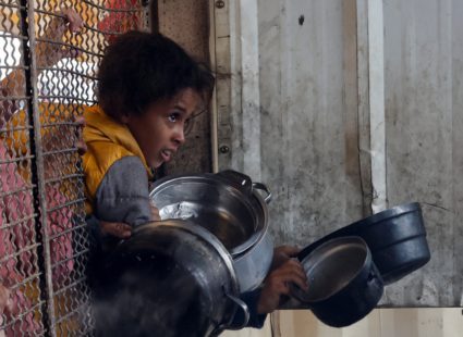 Palestinians queue to receive food cooked by a charity kitchen, in Khan Younis