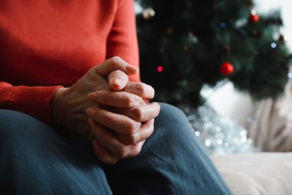 Lonely senior woman sitting at home in Christmas celebration. Close-up of an elderly woman's hand against background of de...