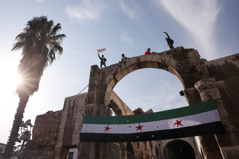 People wave flags during celebrations after Friday prayers, outside the Umayyad Mosque, in Damascus