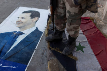 Fighters of the ruling Syrian body steps on a Syrian flag under Bashar al-Assad rule in Aleppo