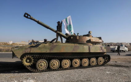 FILE PHOTO: A rebel fighter stands atop a military vehicle as he carries a Hayat Tahrir al-Sham flag in Saraqeb