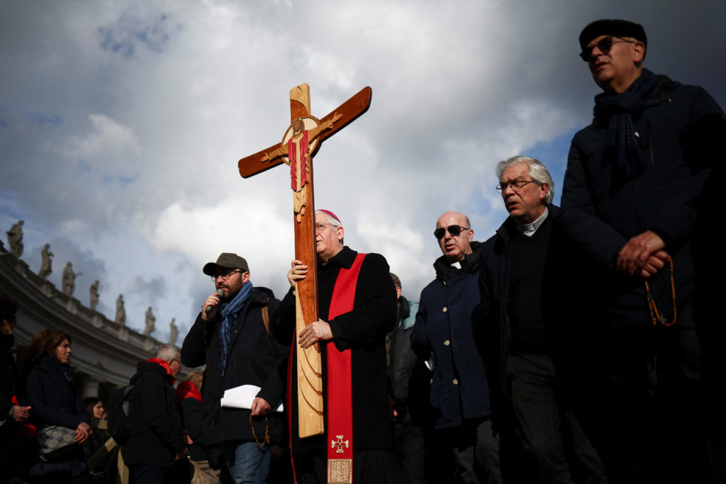 A bishop carries a cross at St. Peter's Square at the Vatican, as Pope Francis continues his hospitalization