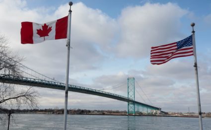 A Canadian and a U.S. flag fly next to the Ambassador Bridge towards Detroit from Windsor, Ontario