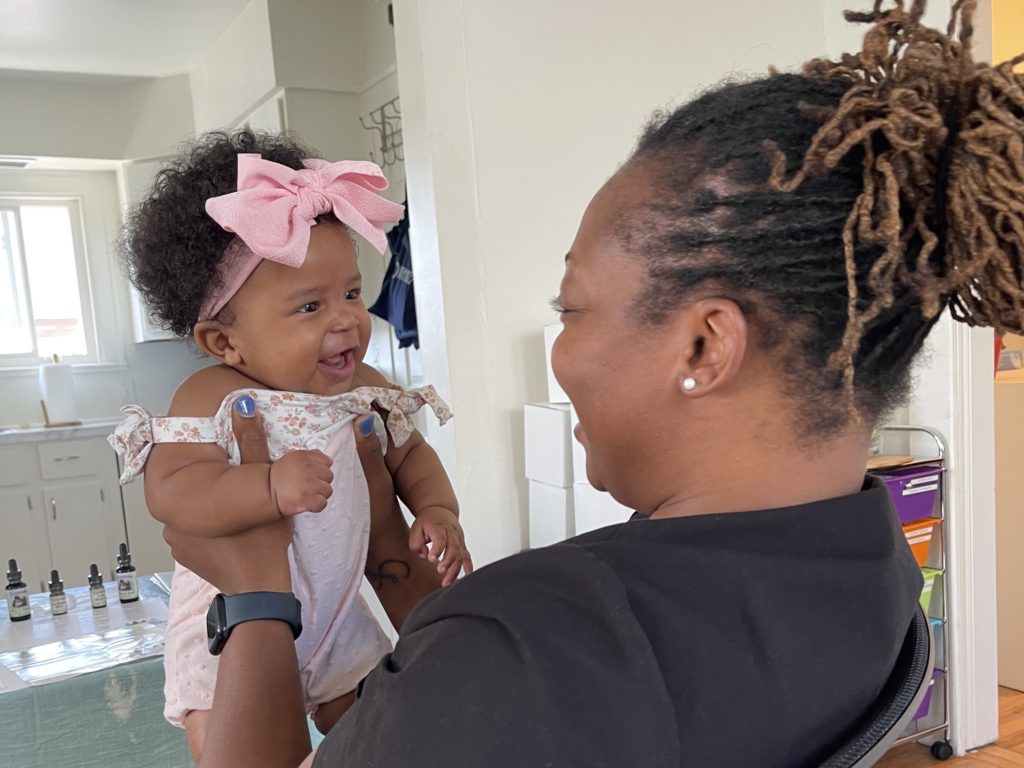 Birth Detroit Midwife Eliken Amable-Brumfield holding and looking at a smiling baby