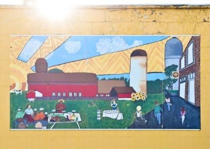 Mural of a farm with barn, grain silo, flowers, garden stand with vegetables, with Ypsilanti's iconic water tower and historic fire house museum