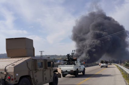 Smoke rises while members of the Syrian forces ride on a vehicle in Latakia