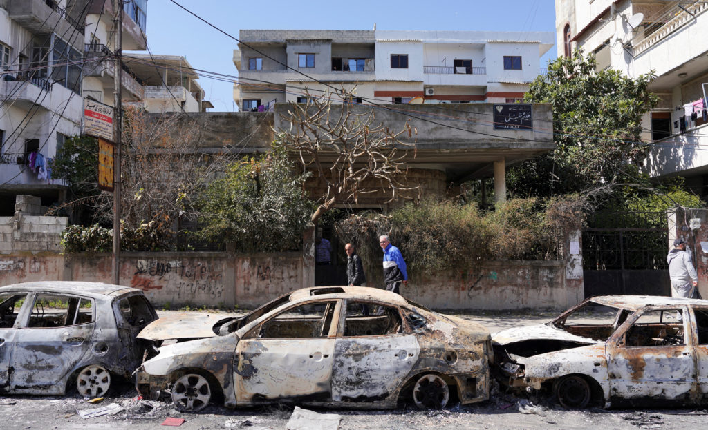 FILE PHOTO: People walk past damaged vehicles in Jableh