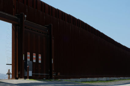 A member of the U.S. Military stands at a gate opening between the border walls sepparating Mexico and the United States, ...