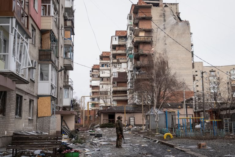 A Ukrainian serviceman stands near residential buildings damaged by Russian military strikes in the frontline town of Pokr...