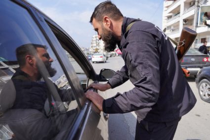 A member of the Syrian security forces checks a car, in Latakia