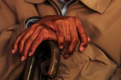 An elderly man crosses his hands on a cane during a funeral in the Bronx borough of New York City