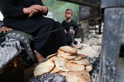 A Palestinian boy sits near a woman baking bread in an oven at a school shelter for displaced people at the Beach camp in ...