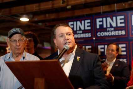 Randy Fine, Republican nominee for 2025 Florida's 6th congressional district, speaks on election night at a podium. Behind him are supporters and Blue campaign signs with the name "FINE" in big white lettering