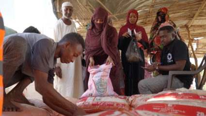 A staff member distributes food items to people displaced due to conflict, in Kassala