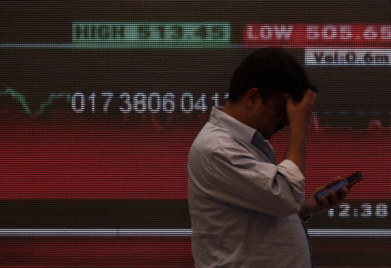 FILE PHOTO: A man stands in front of a screen displaying news of markets update inside the Bombay Stock Exchange (BSE) bui...