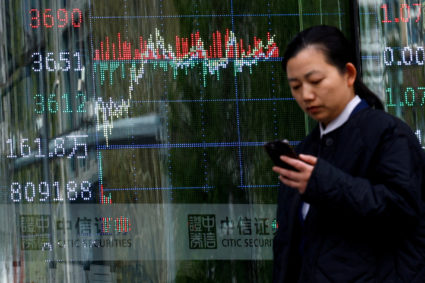 FILE PHOTO: Woman walks past a brokerage house with a display board showing the stock index information, in Beijing