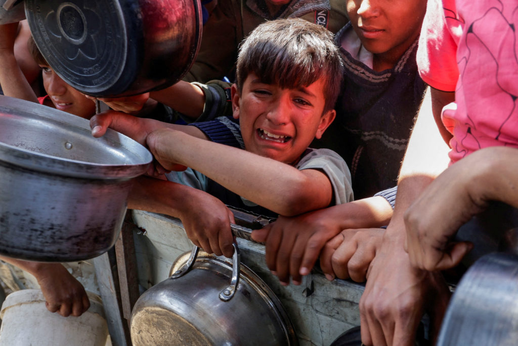 Palestinians wait to receive food cooked by a charity kitchen, in Khan Younis