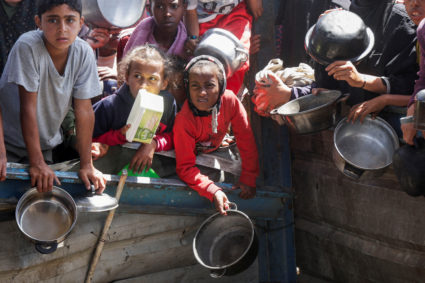 Palestinians wait to receive food cooked by a charity kitchen, in Khan Younis