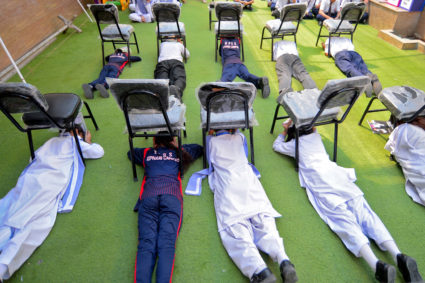 Students use chairs to cover their heads inside a classroom at a school during a mock drill for handling war situations, i...