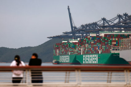 People look on as cargo ships carrying containers are seen in the background near Yantian port in Shenzhen, Guangdong