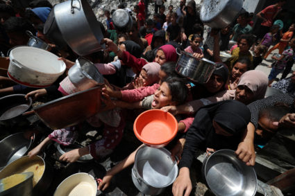 Palestinians wait to receive food cooked by a charity kitchen, in Jabalia, in the northern Gaza Strip